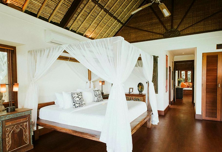 A four-poster bed with mosquito netting under a high palm-thatch ceiling